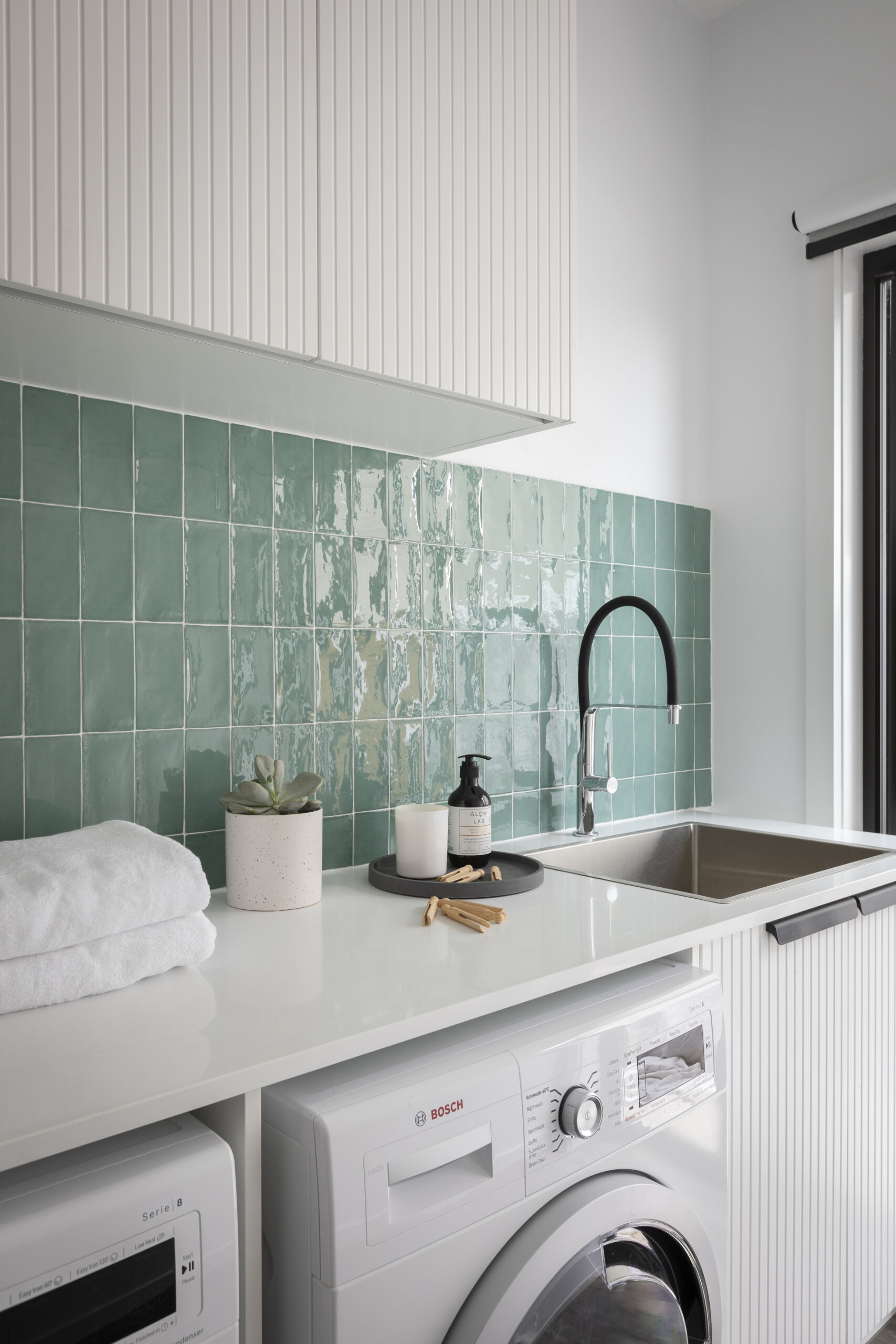 Laundry design trends add a pop of colour through the splashback. 