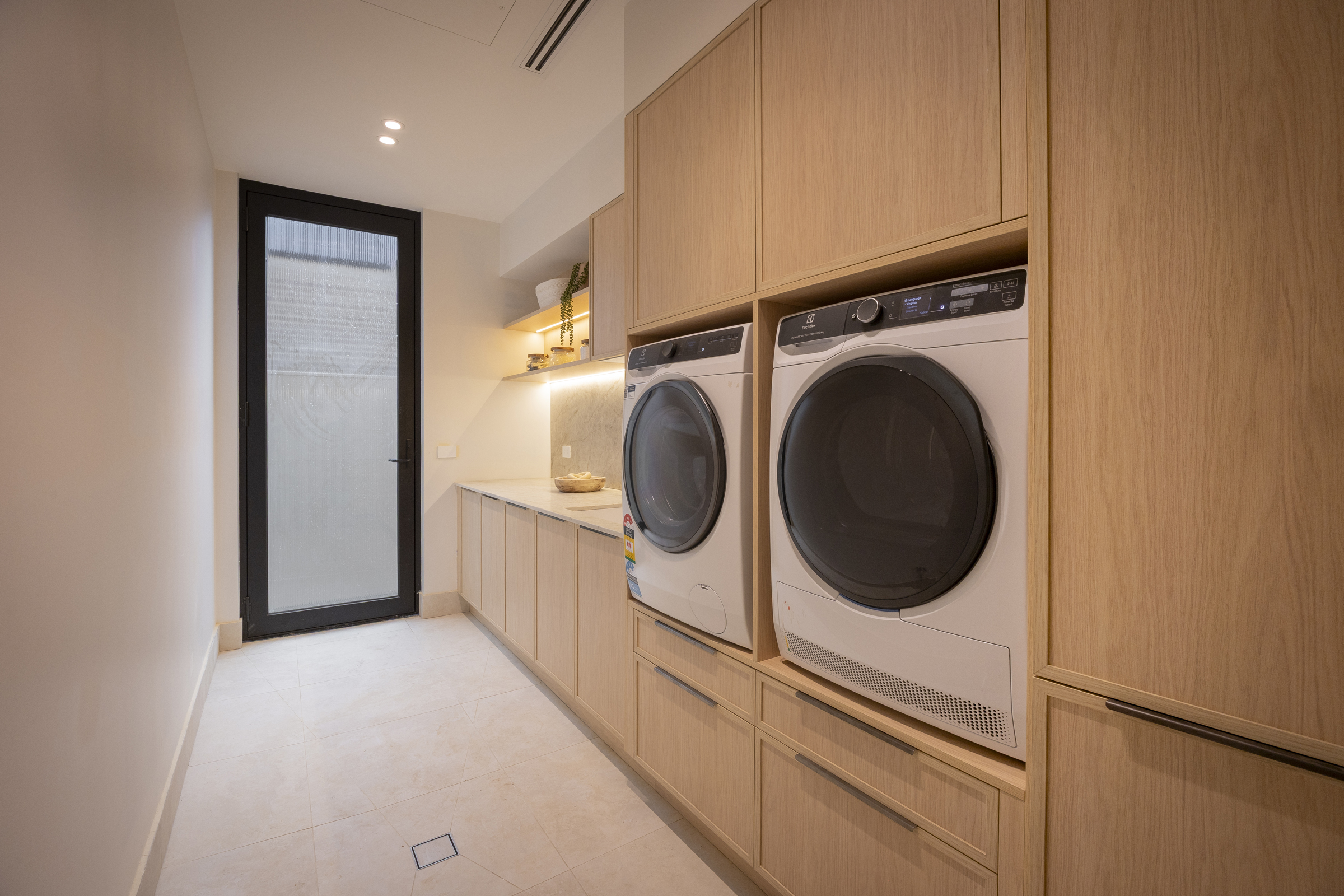 Narrow laundry with raised washer and dryer built into timber-look cabinetry