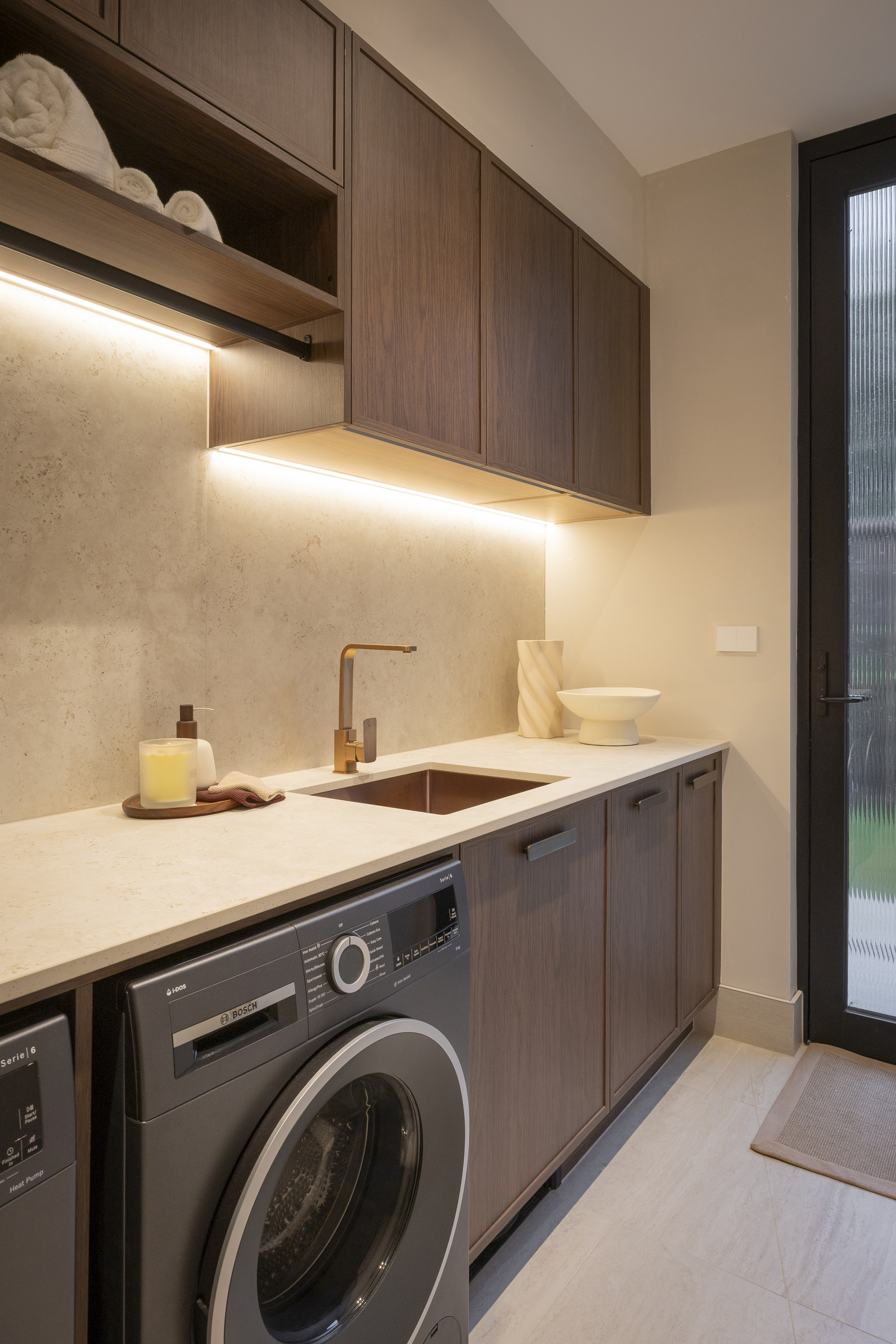 Laundry set up with hanging rail, LED strip lighting under wall cabinets, bench space and laundry appliances