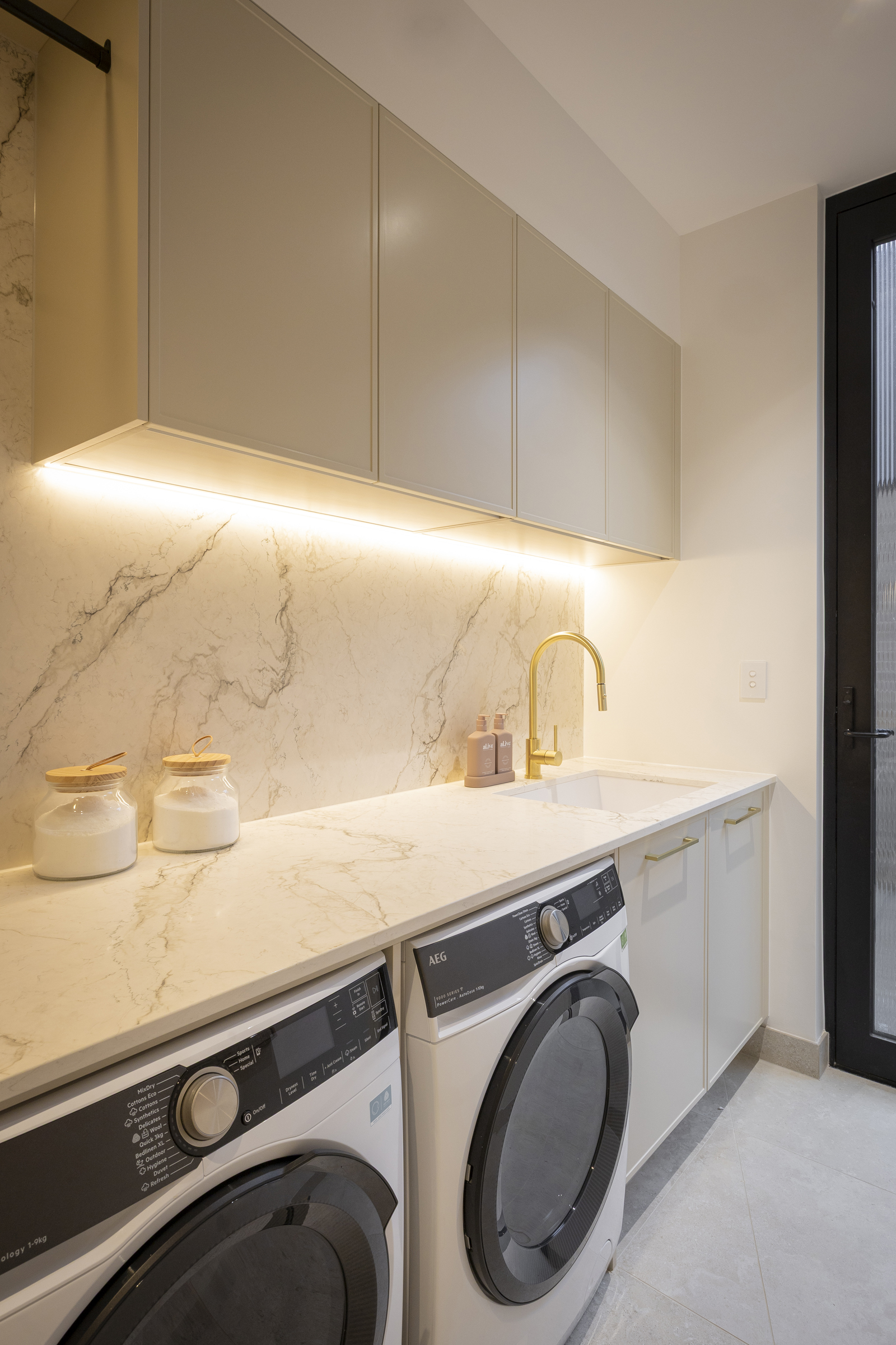 Close of laundry set up with applainces side by side under a large benchtop and wall cabinets