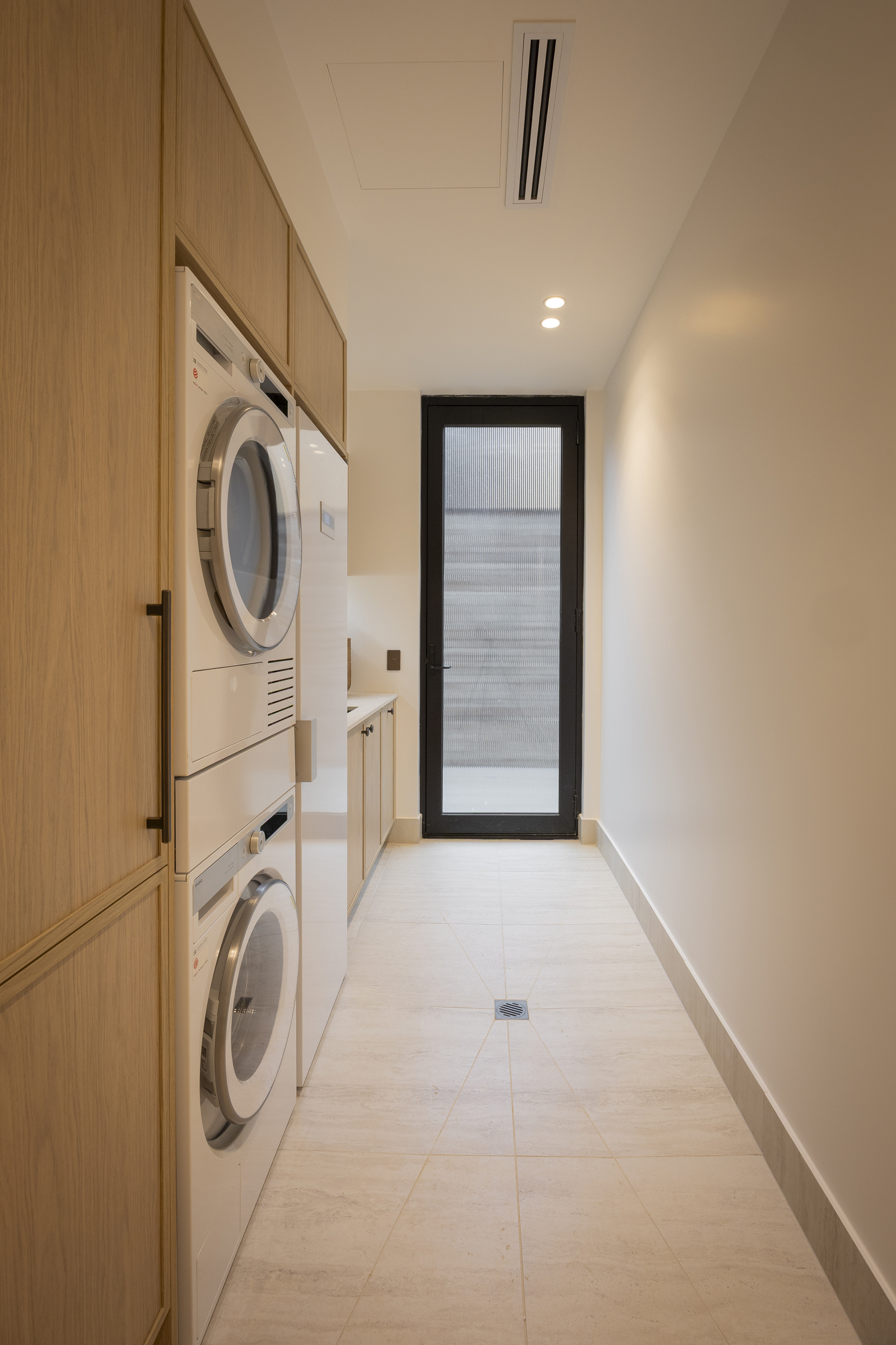 Timber look galley laundry room with tall cabinets and stacked washer and dryer