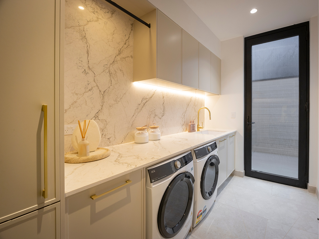 Close-up of Kinsman laundry sink in marble-look stone with brass mixer tap and matching brass cabinetry handles.