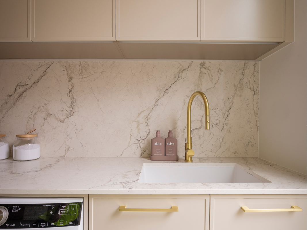Kinsman laundry featuring dramatic marble-look splashback, brass hardware, floating overhead cabinetry and undermount sink