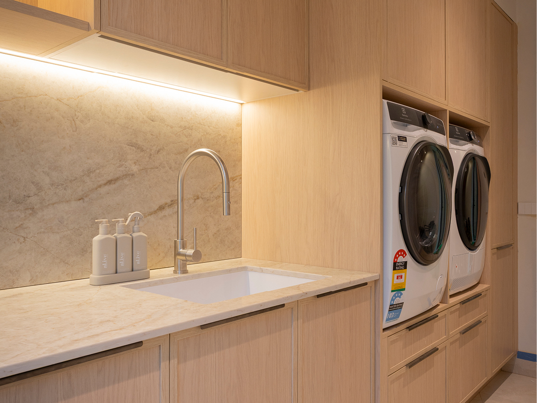 Close-up of Kinsman laundry benchtop with undermount sink, brushed tapware, stone-inspired splashback and under-cabinet lighting.