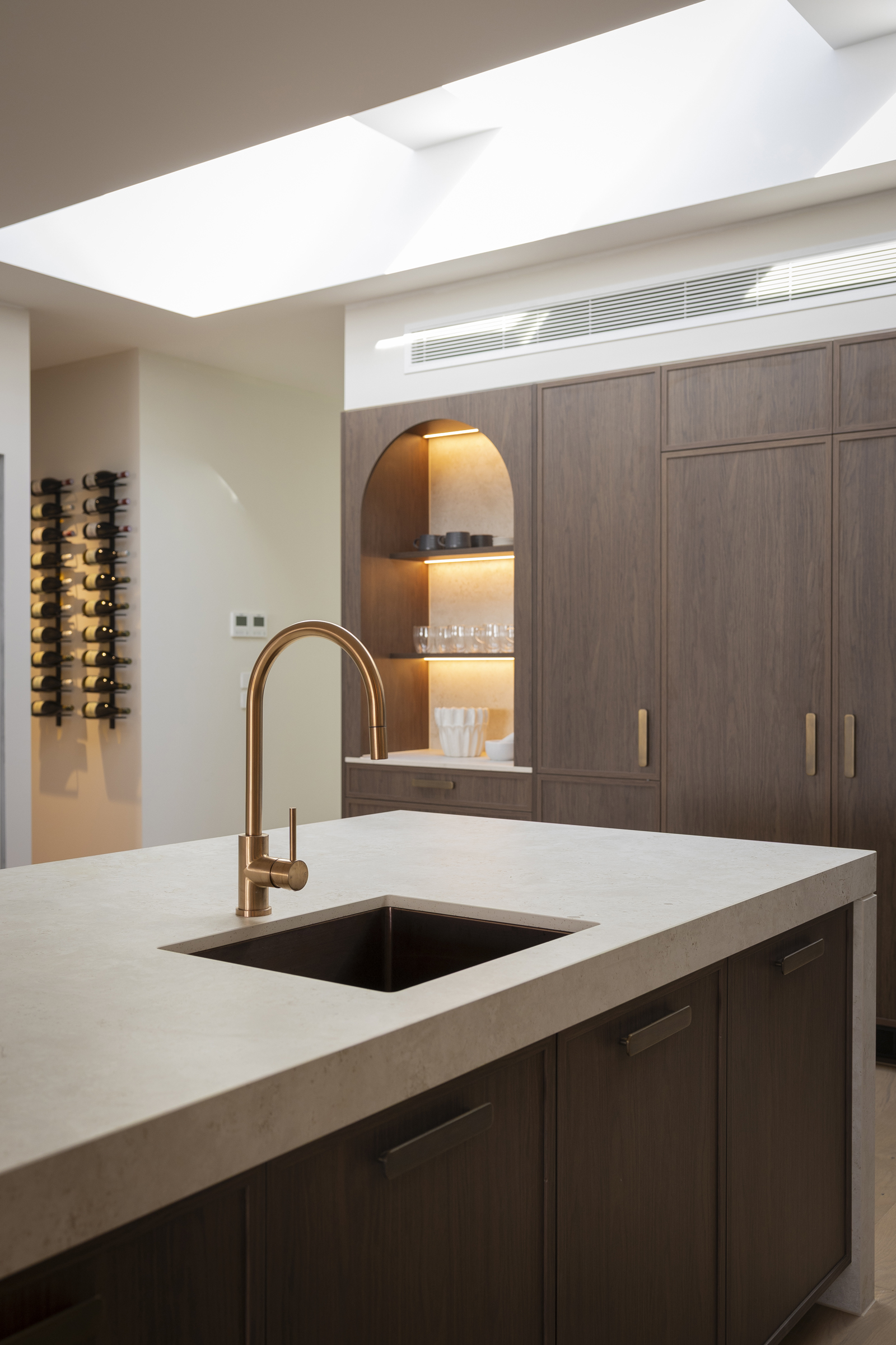 Dekton Sabbia island benchtop with sink, brass tapware and dark timber-look cabinetry